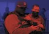 Arlington County Sues to Block Armed Federal Agents at Polls Two masked law-enforcement officers in tactical vests stand at a polling place, one pointing while the other holds a phone, in a red-and-blue duotone photo.