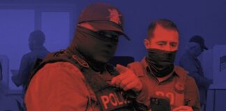 Two masked law-enforcement officers in tactical vests stand at a polling place, one pointing while the other holds a phone, in a red-and-blue duotone photo.