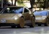 Tesla Profit Falls 43% in Third Quarter; Cybercab Joins Robotaxi Fleet Two gold Tesla Cybercabs drive down a tree-lined street while people on the sidewalk take photos.