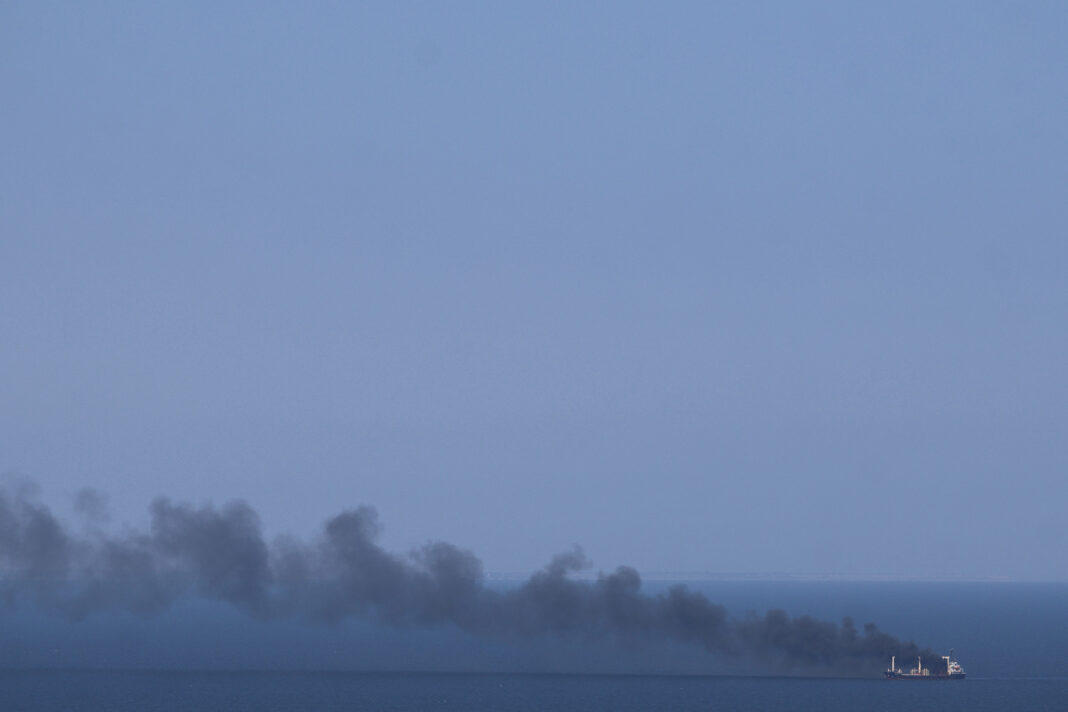 Merchant ship trailing a long plume of black smoke at sea under a hazy sky, illustrating calls for a Black Sea naval operation