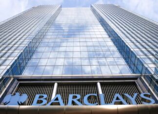 Barclays Cutting 5,000 Jobs in AI-Driven Cost Push A low-angle view looking up at the glass Barclays headquarters tower, with the blue Barclays sign at the bottom. (Screenshot)