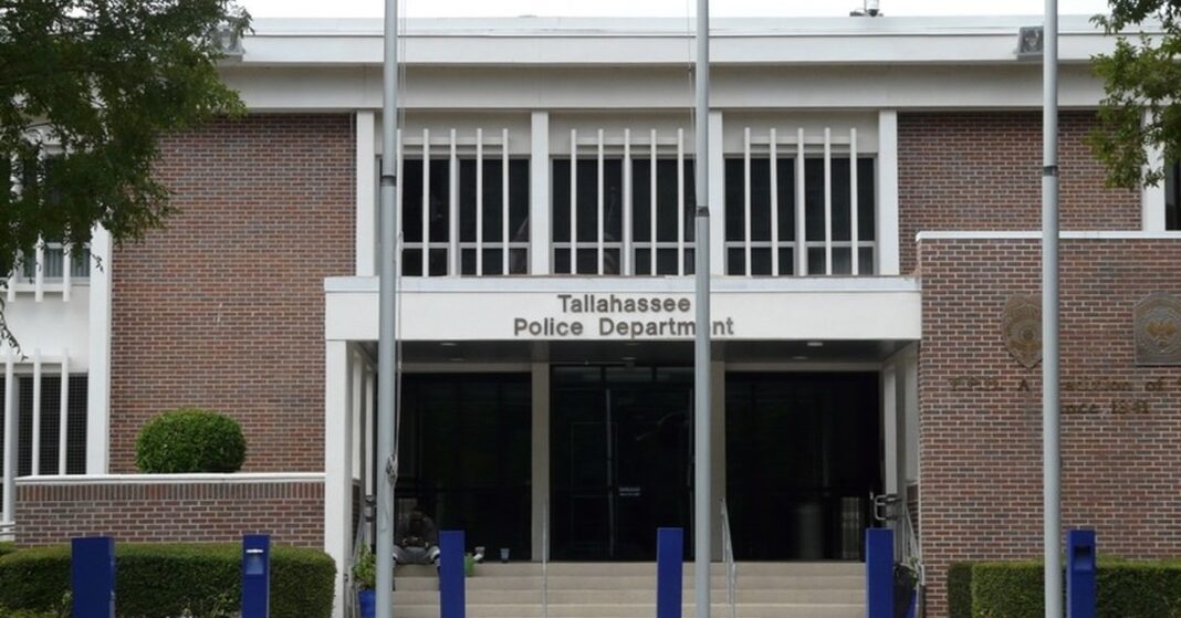 Front entrance of the brick Tallahassee Police Department headquarters building with blue bollards and flagpoles
