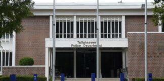 Front entrance of the brick Tallahassee Police Department headquarters building with blue bollards and flagpoles