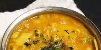 Aloo Tama Bodi curry in a metal bowl, with potato pieces, black-eyed peas and chopped herbs in a golden broth.