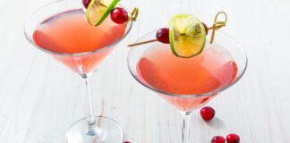 Two pink Cosmopolitan cocktails in martini glasses garnished with lime wheels and cranberries on cocktail picks