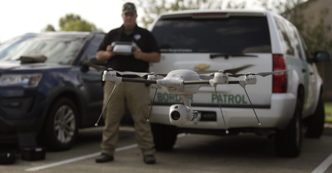A U.S. Border Patrol agent tests a small drone in front of a Border Patrol vehicle