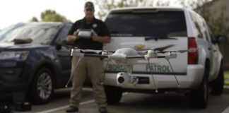 A U.S. Border Patrol agent tests a small drone in front of a Border Patrol vehicle