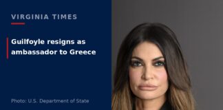 Official portrait of Kimberly Guilfoyle, U.S. ambassador to Greece, wearing a black suit with a U.S. flag behind her