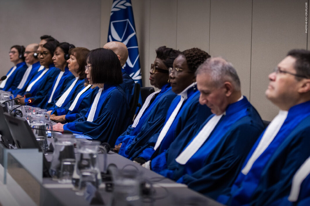 Sakharov Prize laureate International Criminal Court judges in blue and white robes seated at the bench in front of an ICC flag
