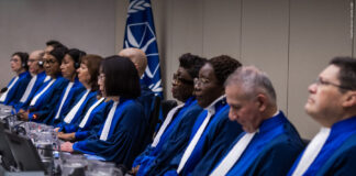 Sakharov Prize laureate International Criminal Court judges in blue and white robes seated at the bench in front of an ICC flag