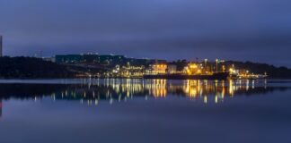 The Preemraff oil refinery and storage tanks in Sweden lit at blue hour, reflected in calm water