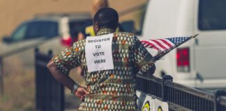 Noncitizen voter subpoenas: a voter registration volunteer wearing a "Register to Vote Here" sign in North Minneapolis (file photo)