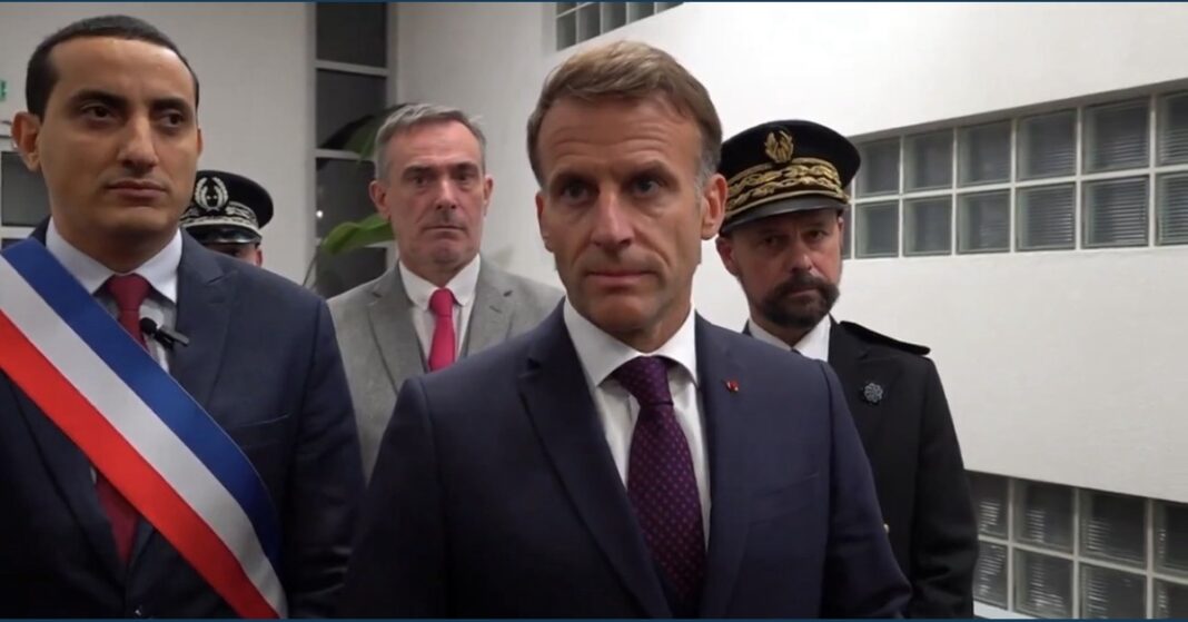 French President Emmanuel Macron stands with officials while delivering a statement in Trappes.
