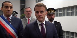 French President Emmanuel Macron stands with officials while delivering a statement in Trappes.