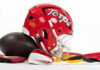 Maryland football helmet bearing the Terps script beside a football on red, white, black and gold fabric.