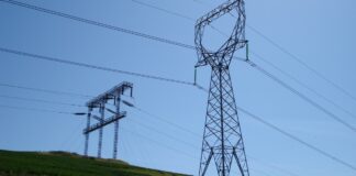 High-voltage electricity transmission towers and power lines on a grassy hillside under a clear blue sky