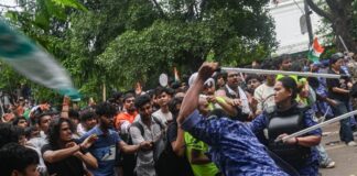 Police officers holding batons face a crowd of demonstrators during a student protest in New Delhi.