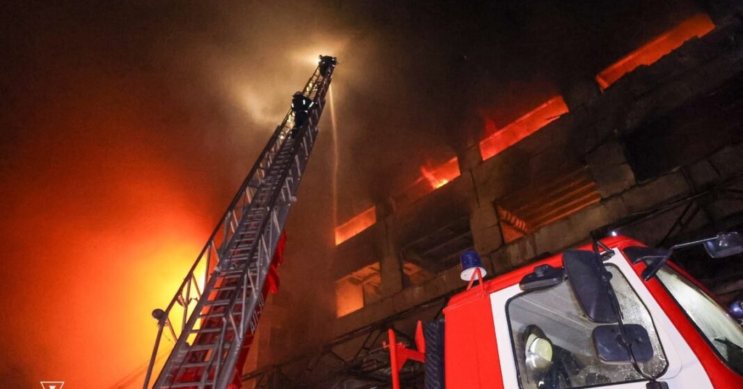 Firefighters on an extended ladder spray water on a burning multistory building at night in Ukraine's Kharkiv region as a fire truck stands below.