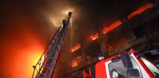 Firefighters on an extended ladder spray water on a burning multistory building at night in Ukraine's Kharkiv region as a fire truck stands below.