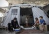 WFP Cuts Gaza Food Aid by a Third as Money Runs Short Woman preparing food outside a tent with children in Al Saraya Camp, pictured in WFP’s Gaza food aid release.