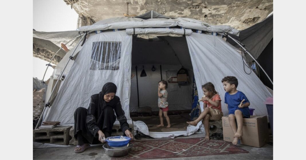Woman preparing food outside a tent with children in Al Saraya Camp, pictured in WFP’s Gaza food aid release.