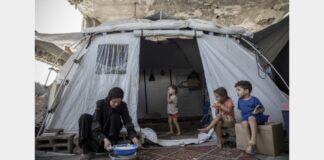 Woman preparing food outside a tent with children in Al Saraya Camp, pictured in WFP’s Gaza food aid release.