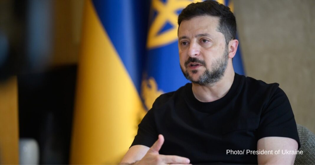 Ukrainian President Volodymyr Zelenskyy speaks during an interview, with Ukrainian flags behind him.