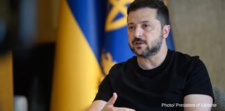 Ukrainian President Volodymyr Zelenskyy speaks during an interview, with Ukrainian flags behind him.